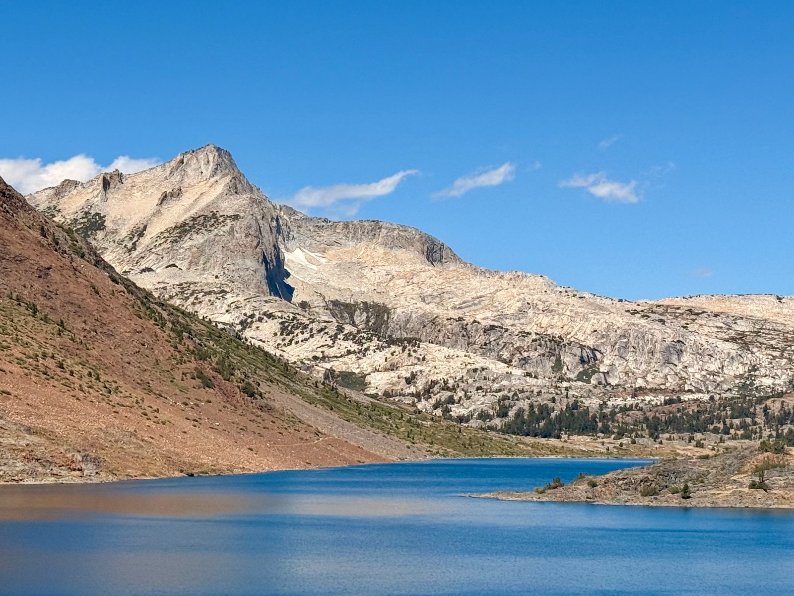 White granite of North Peak rising over the deep blue of Saddlebag Lake, a slope of red talus running down to the water. Twenty Lakes Basin, California.